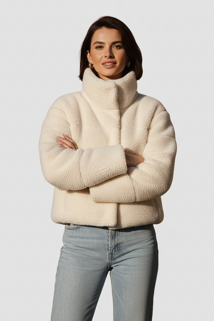 Woman wearing a cream sherpa jacket and light blue jeans on a white background
