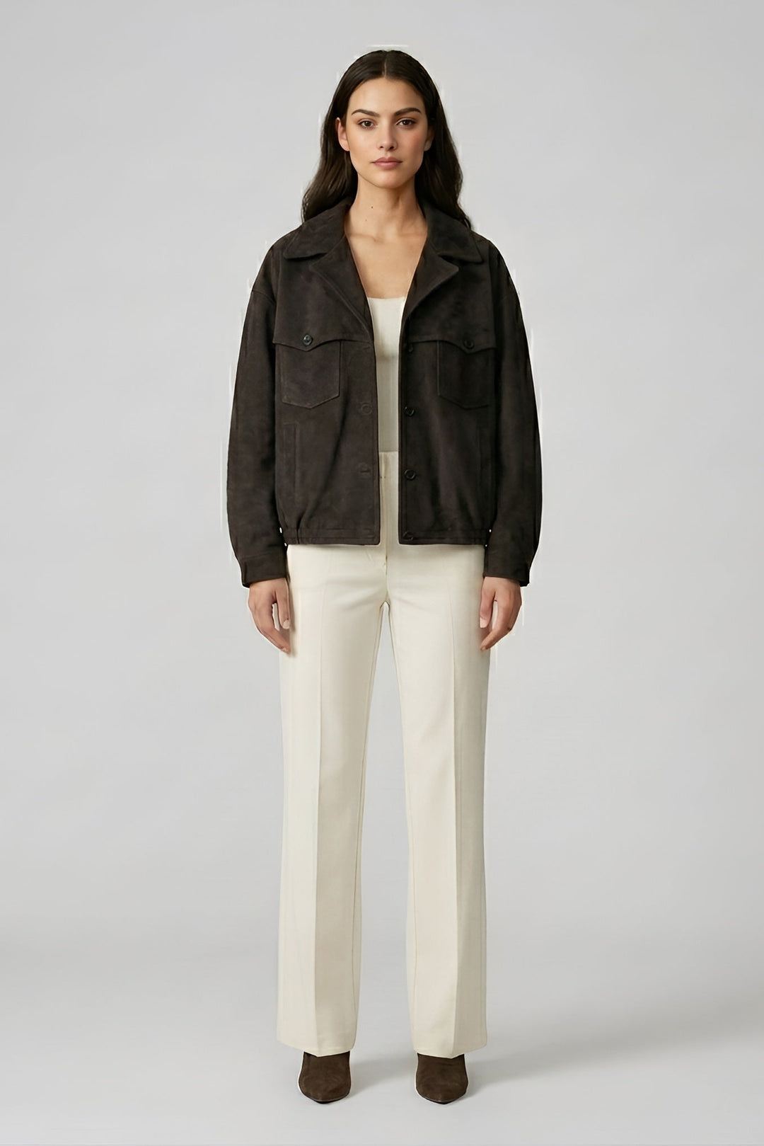 Woman wearing a dark jacket and white pants on a plain background