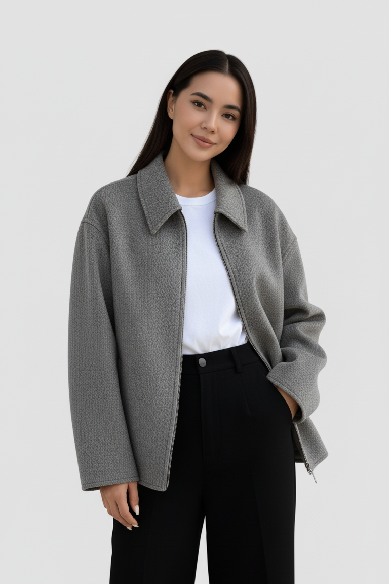 Woman wearing a gray coat over a white shirt and black pants on a plain background