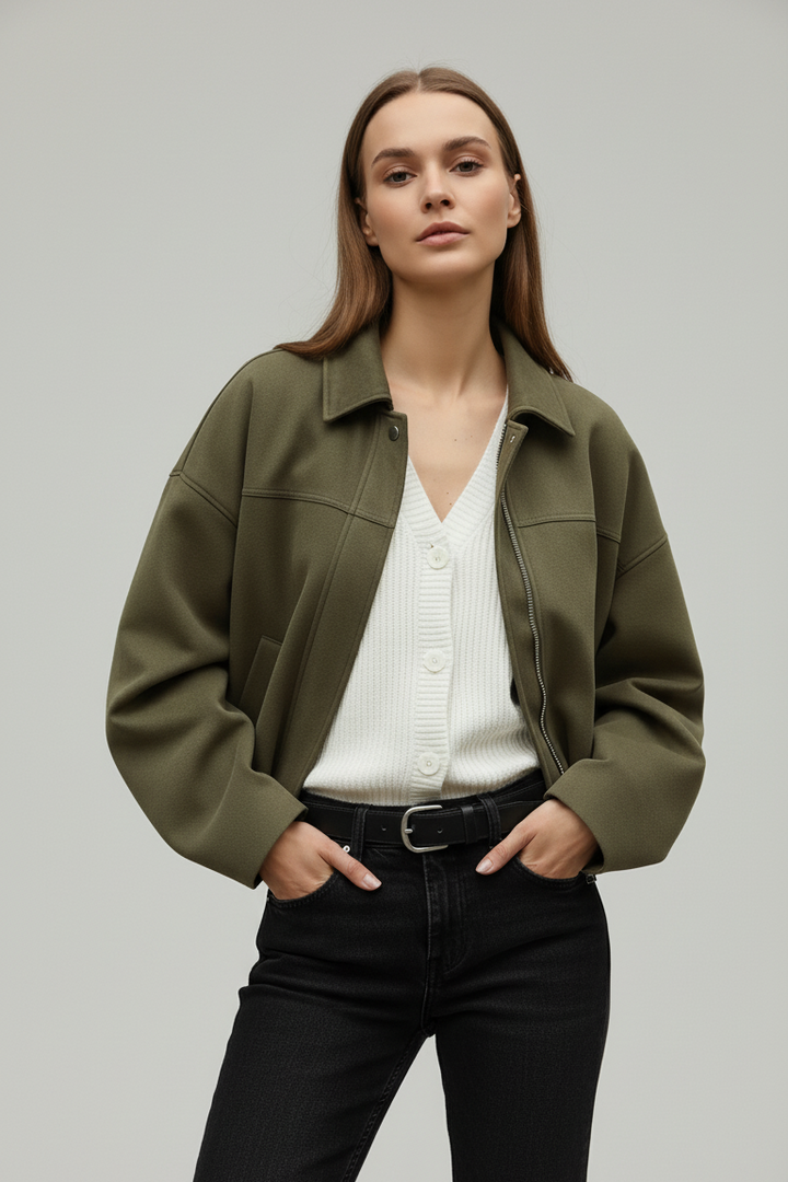 Woman wearing a green jacket over a white shirt and black pants on a plain background