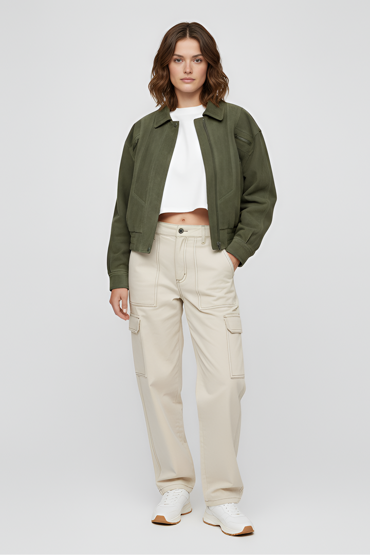 Woman wearing a green jacket, white shirt, beige pants, and white shoes on a light gray background