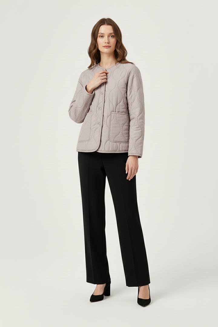 Woman wearing a light gray quilted jacket and black pants on a white background