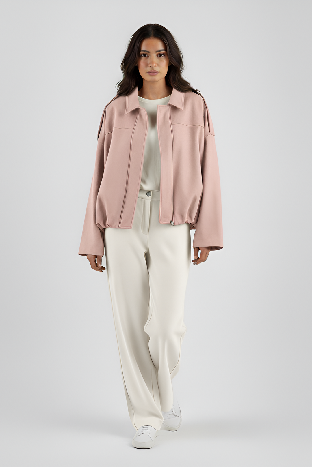 Woman wearing a light pink jacket and white pants on a plain background