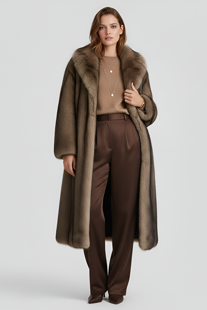 Woman wearing a long brown coat with fur collar and brown pants on a light gray background