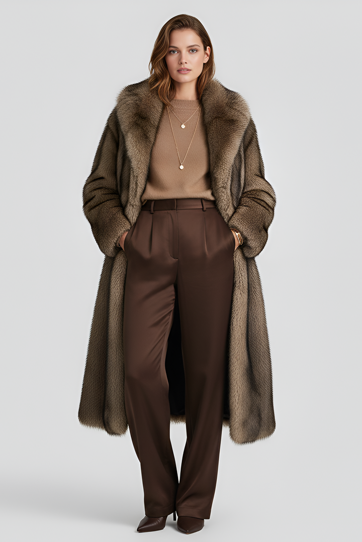 Woman wearing a long brown coat with fur collar and brown pants on a light gray background