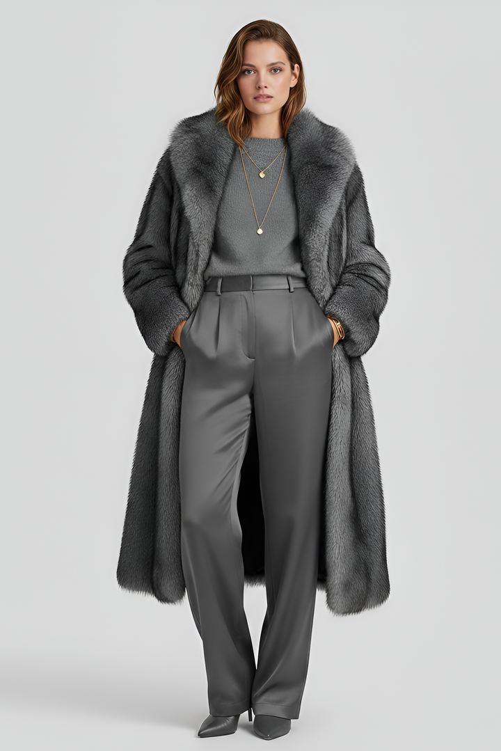 Woman wearing a long gray coat with fur trim on a light gray background