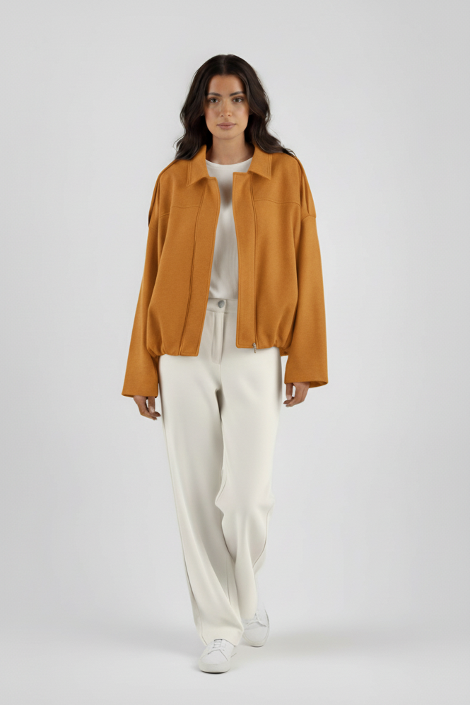 Woman wearing a mustard yellow jacket and white pants on a gray background
