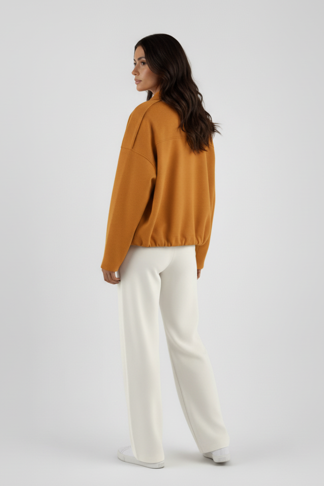 Woman wearing a mustard yellow sweater and white pants on a light gray background