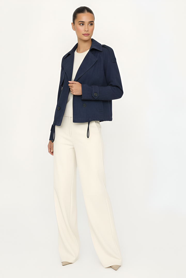 Woman wearing a navy jacket and white pants on a light gray background