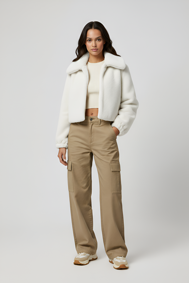 Woman wearing a white coat, beige pants, and white sneakers on a plain background