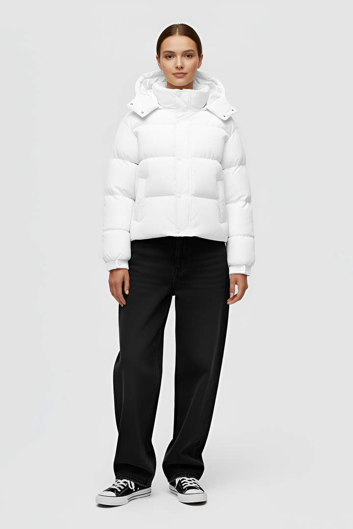 Woman wearing a white puffer jacket and cap standing in an urban setting.