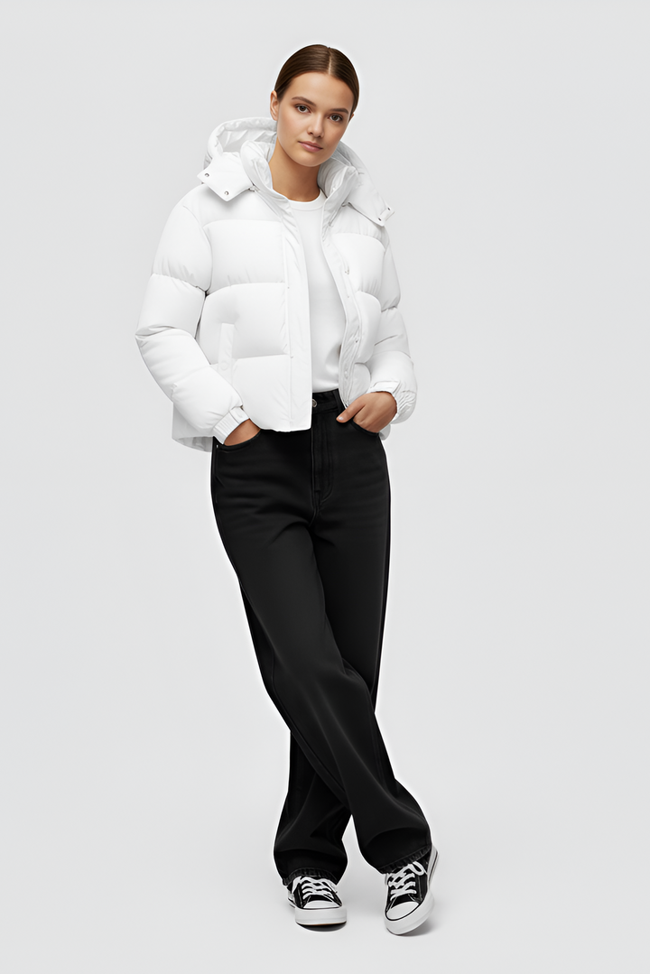 Woman wearing a white puffer jacket and cap standing in an urban setting.