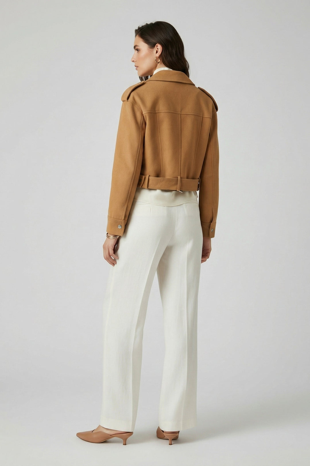 Woman wearing a brown jacket and white pants on a plain background