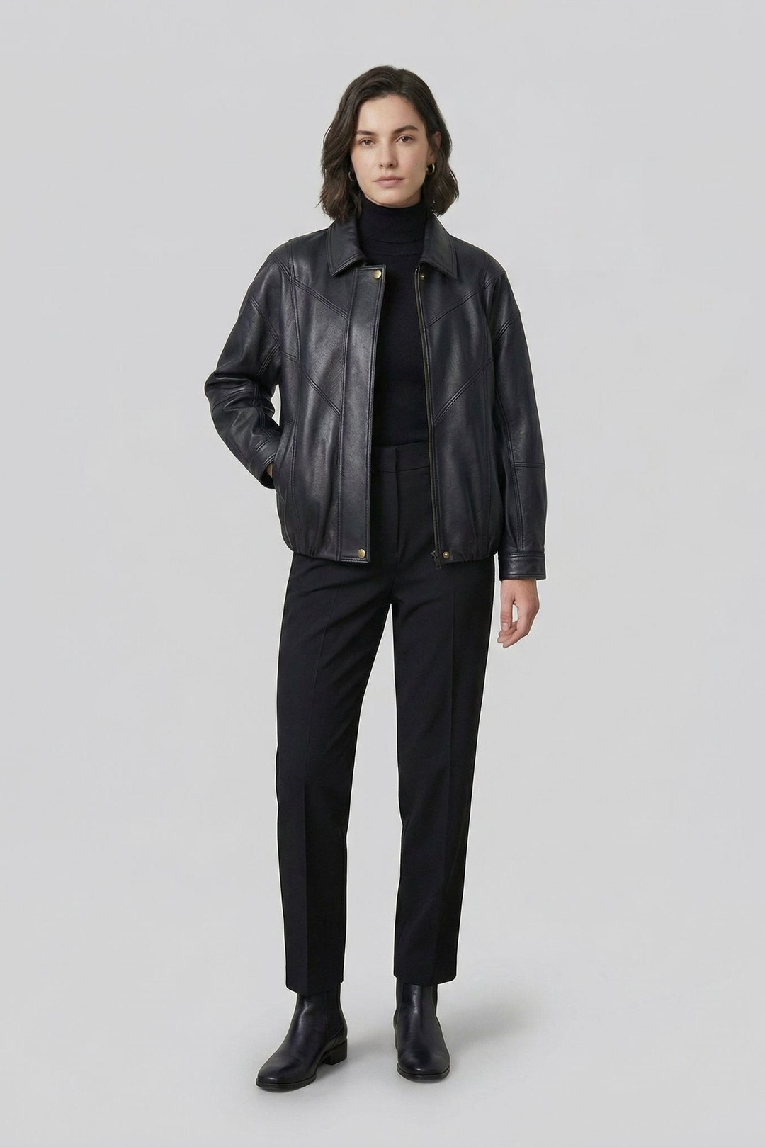 HAILEY - Woman wearing a black leather bomber jacket over a black turtleneck and trousers, front view