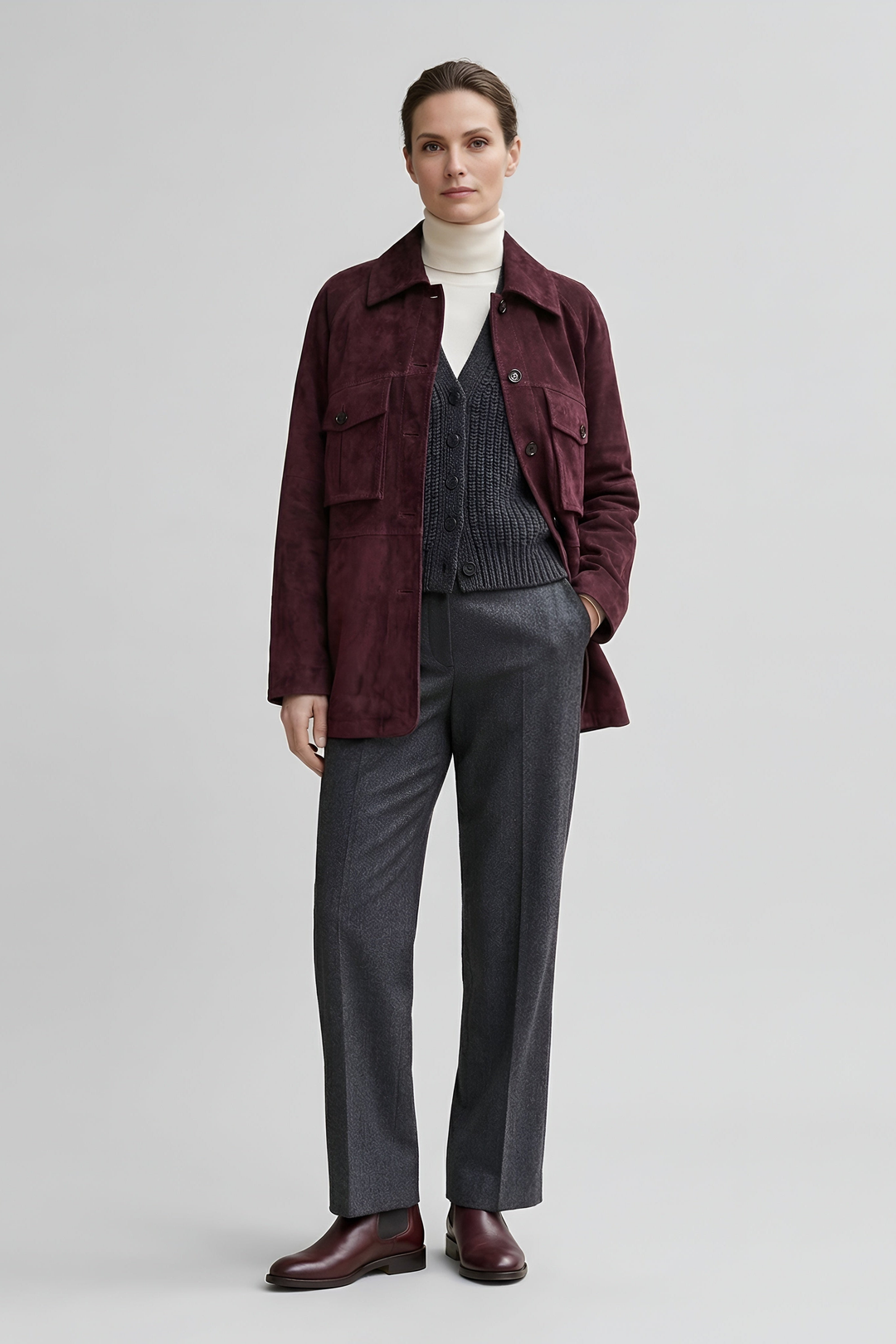 IVY - Woman wearing a burgundy suede shirt jacket over a cream turtleneck and grey knit vest, front view, one hand in pocket